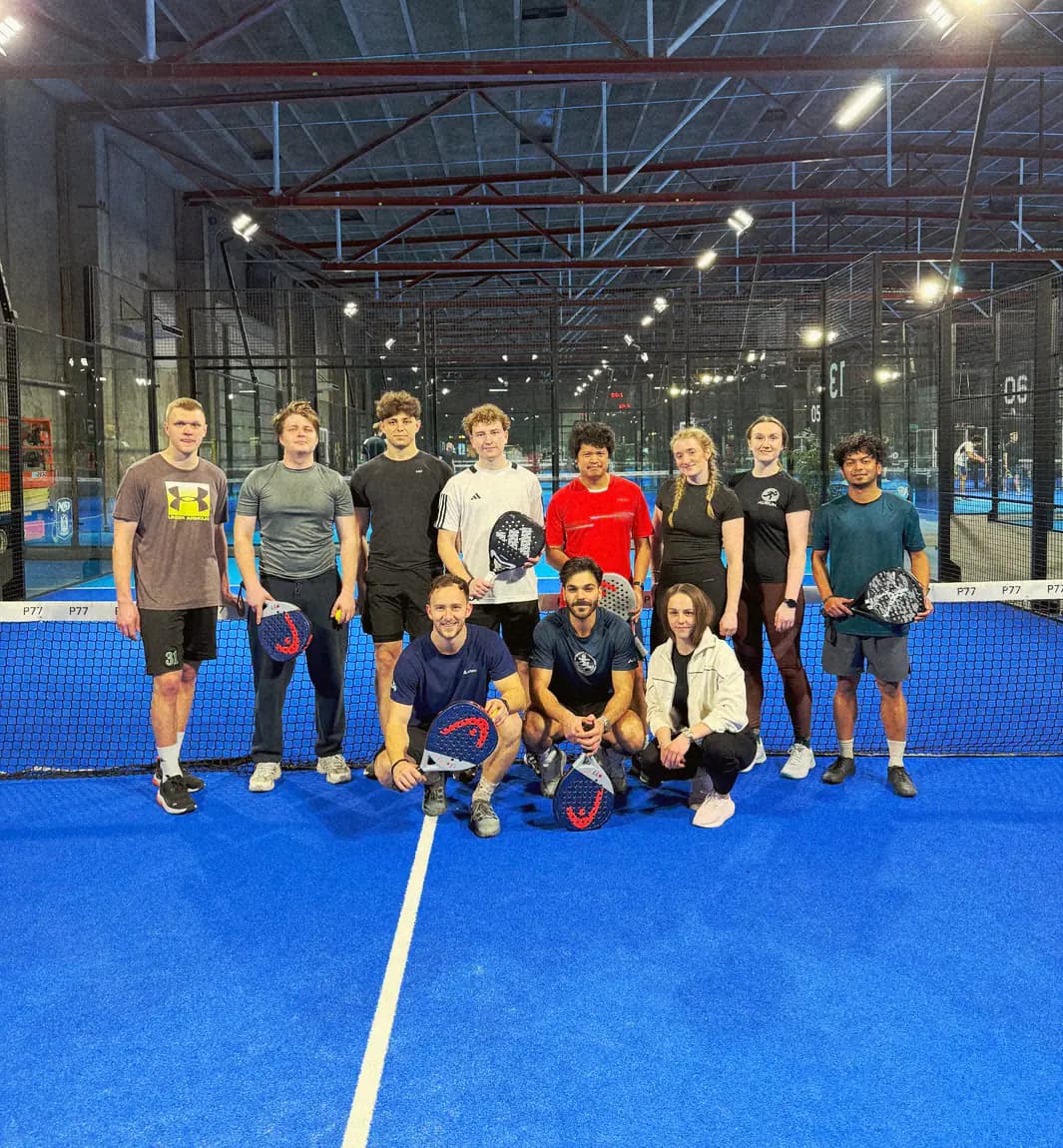 En athme-padelgruppe med ketsjere på en blå indendørsbane i København