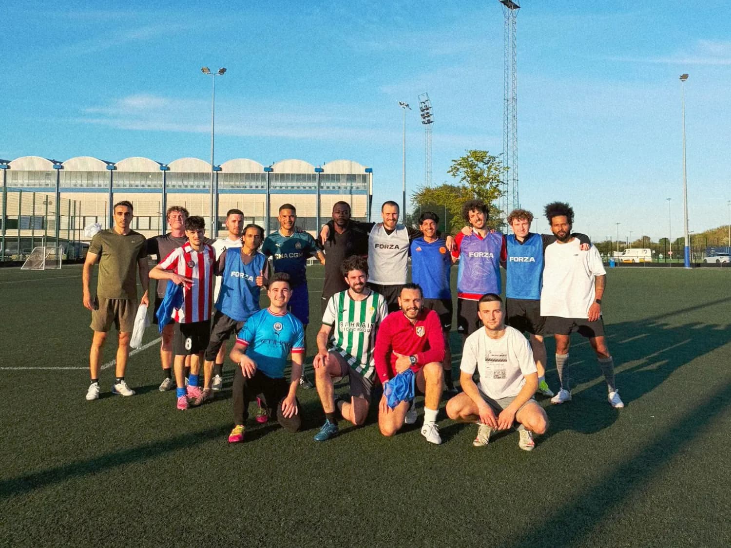 An athme football crew posing together on an artificial pitch after a game, in the evening sun