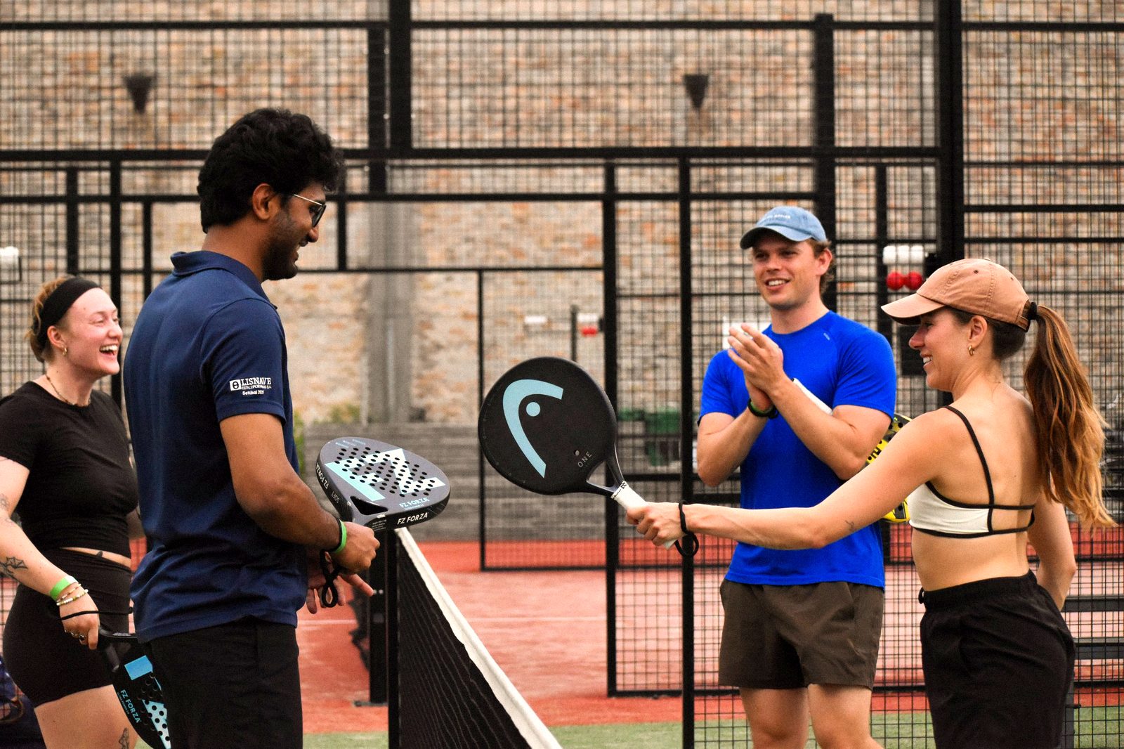 Four players laughing and tapping rackets after a match